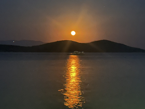 A full moon over a hill with a long golden reflection on the sea