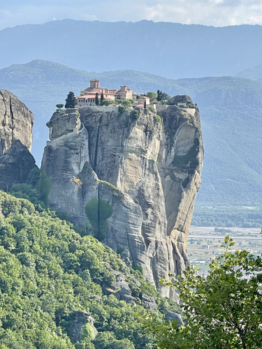 Monastery perched on a sheer rock pillar above green hills