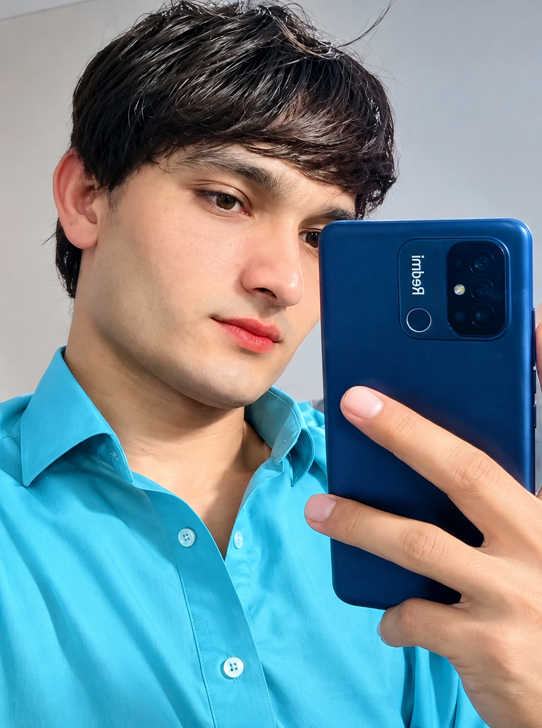 Young man in a turquoise shirt taking a mirror selfie with a blue smartphone