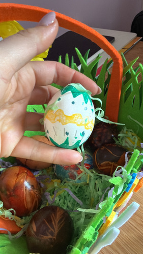 Hand holding a green and yellow painted egg over a basket