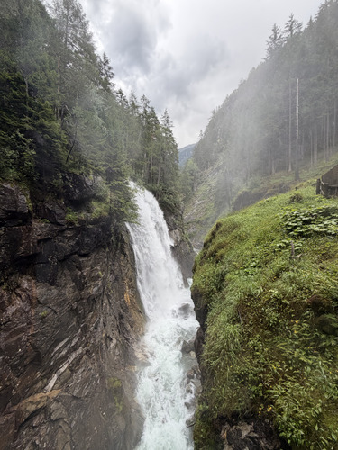 Tall waterfall cascading down a rocky gorge under cloudy skies
