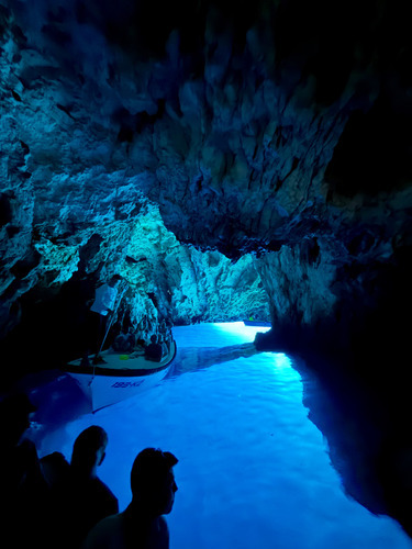 Visitors in a dark sea cave lit by bright blue water