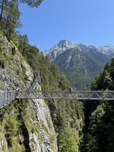 Metal footbridge across a deep gorge with a rocky mountain peak behind