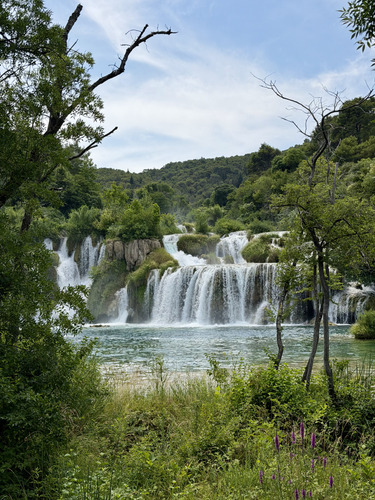 Waterfalls cascading into a green lake surrounded by trees
