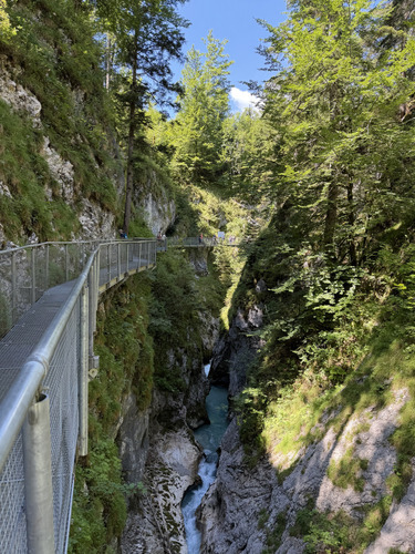 Railed walkway along a cliff above a turquoise river in a wooded gorge