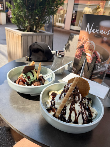 Two bowls of ice cream sundaes with wafers and chocolate sauce at an outdoor table