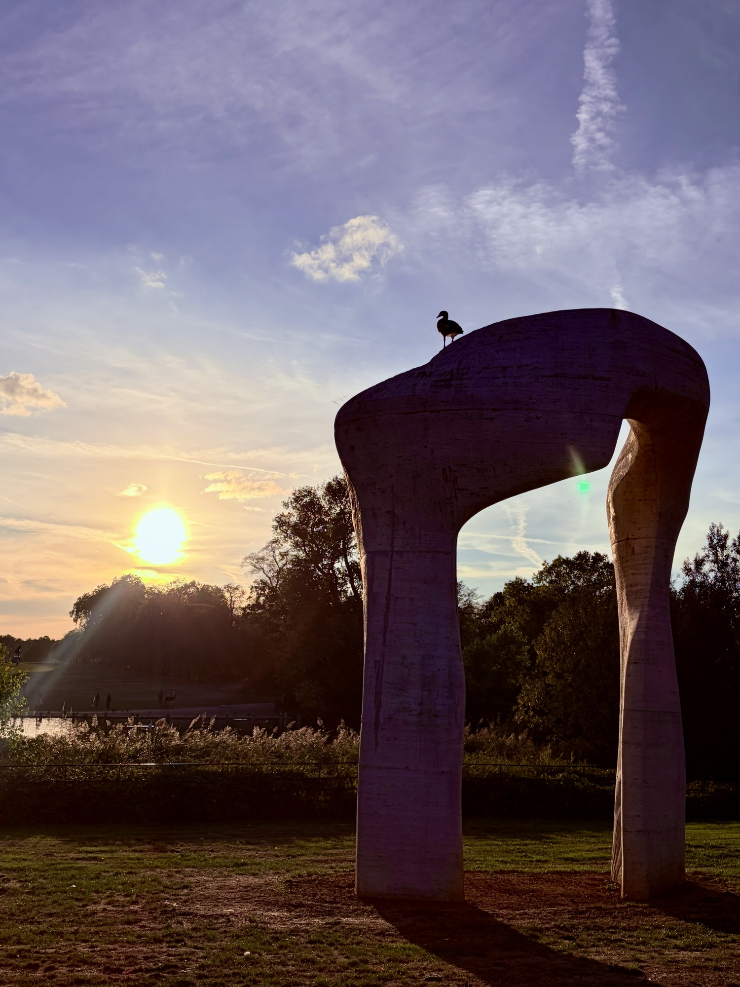Stone arch sculpture with a bird on top, silhouetted against the low sun