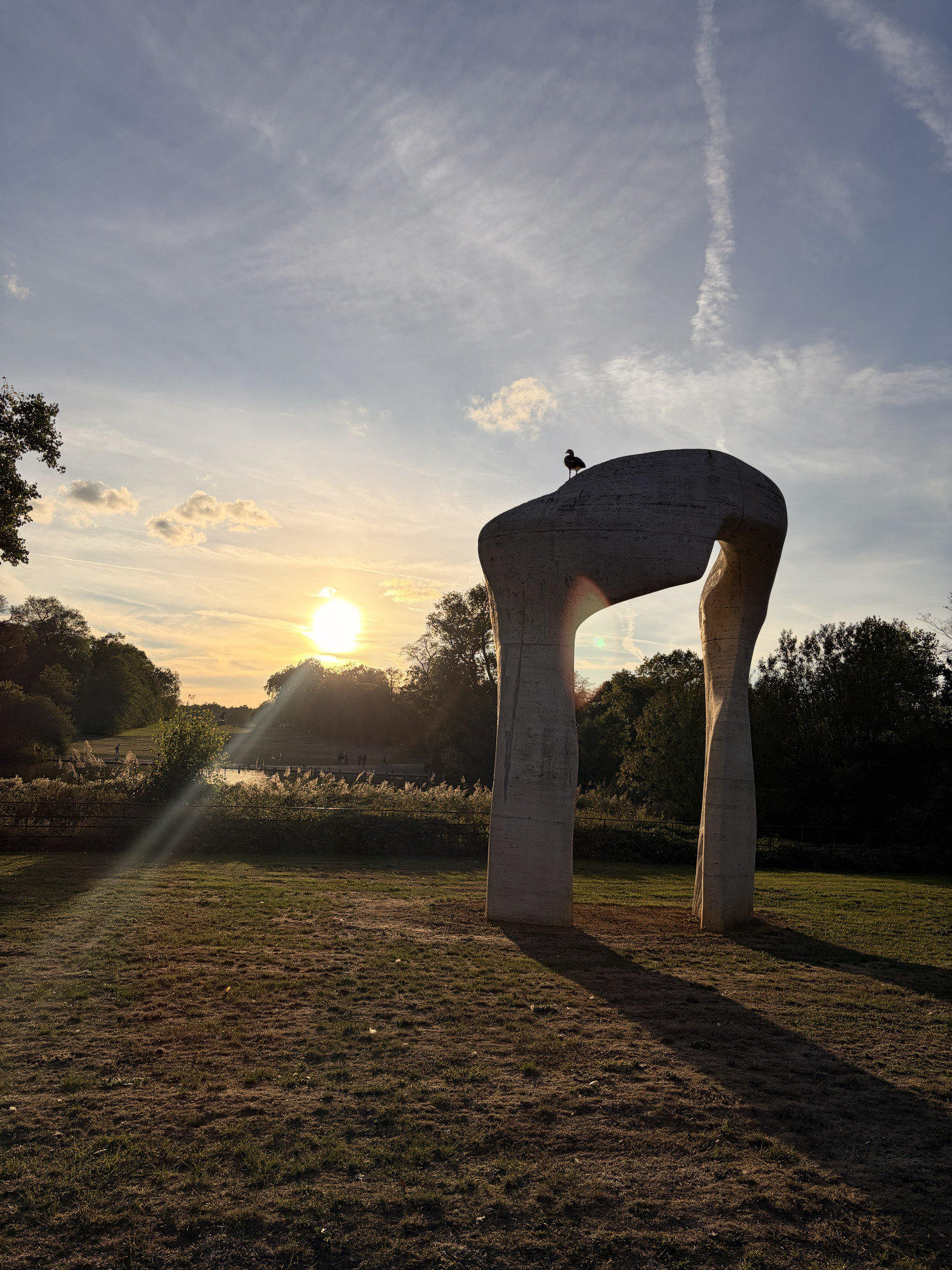 Stone arch sculpture on a lawn casting long shadows at golden hour